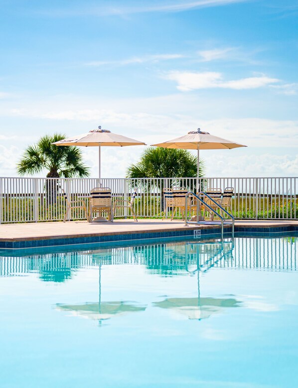 A swimming pool with a white fence, two umbrellas, and lounge chairs.