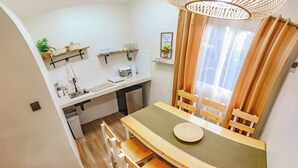 Cocina compacta con alacenas blancas, lavavajillas integrado y comedor con una mesa redonda y sillas de madera.