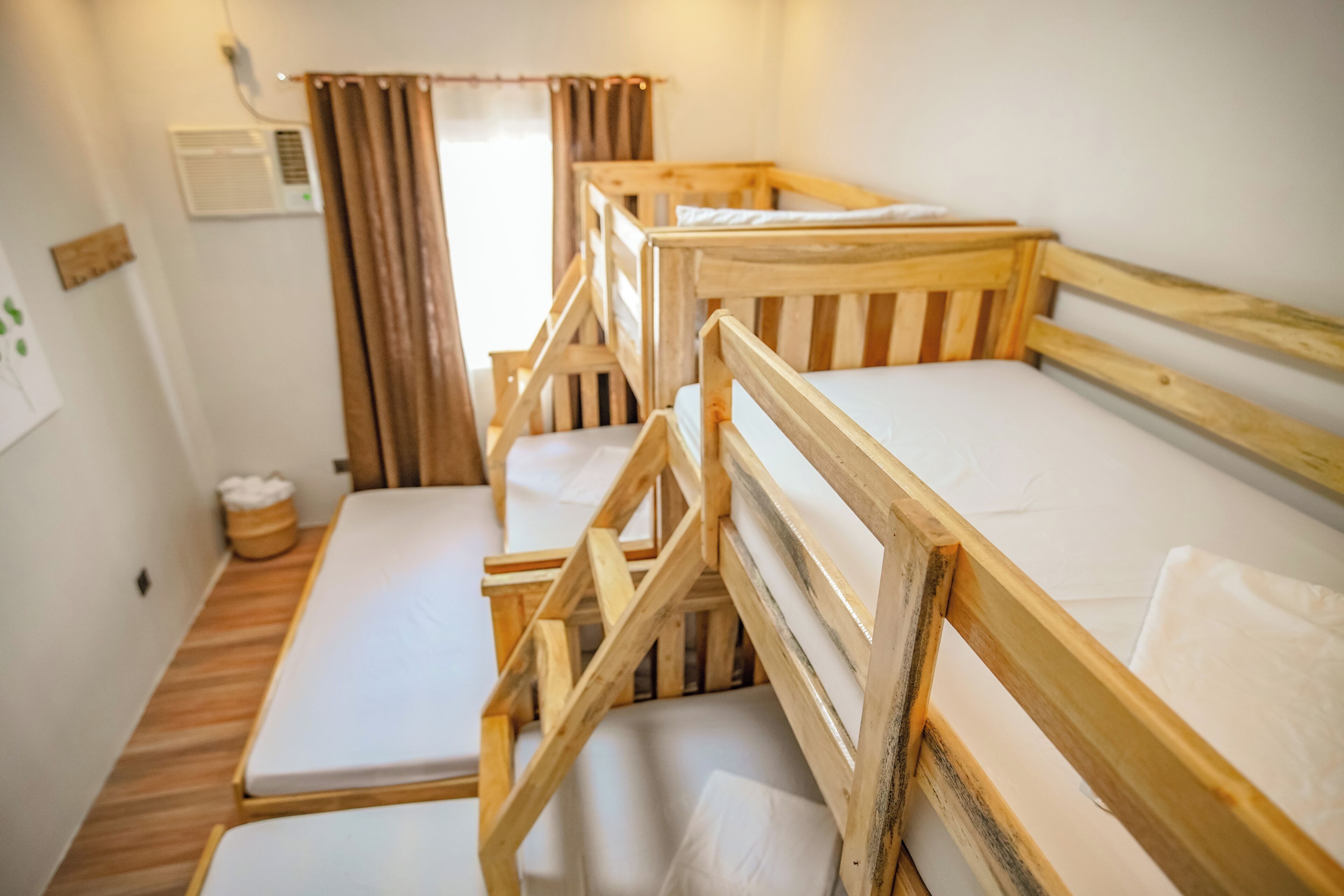 A room with three wooden bunk beds, a small wooden table, and a wall-mounted air conditioning unit.