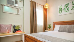 Un dormitorio con una cama de madera, un banco con cojines, una mesita de noche con una planta y un aire acondicionado instalado en la pared.