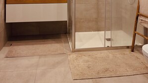 Un baño moderno con cabina de ducha de vidrio, un espejo grande y un tocador de madera.