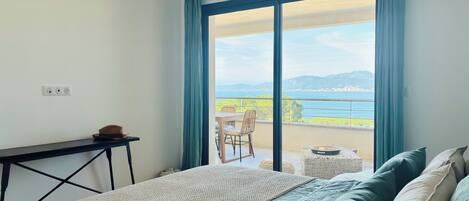 A bedroom with a bed, a desk, and a view of the sea.
