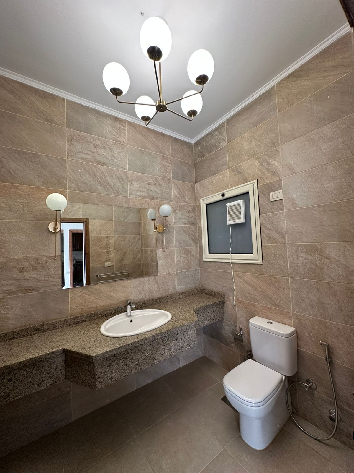 Un baño moderno con lavamanos de granito, inodoro blanco e iluminación en el techo.
