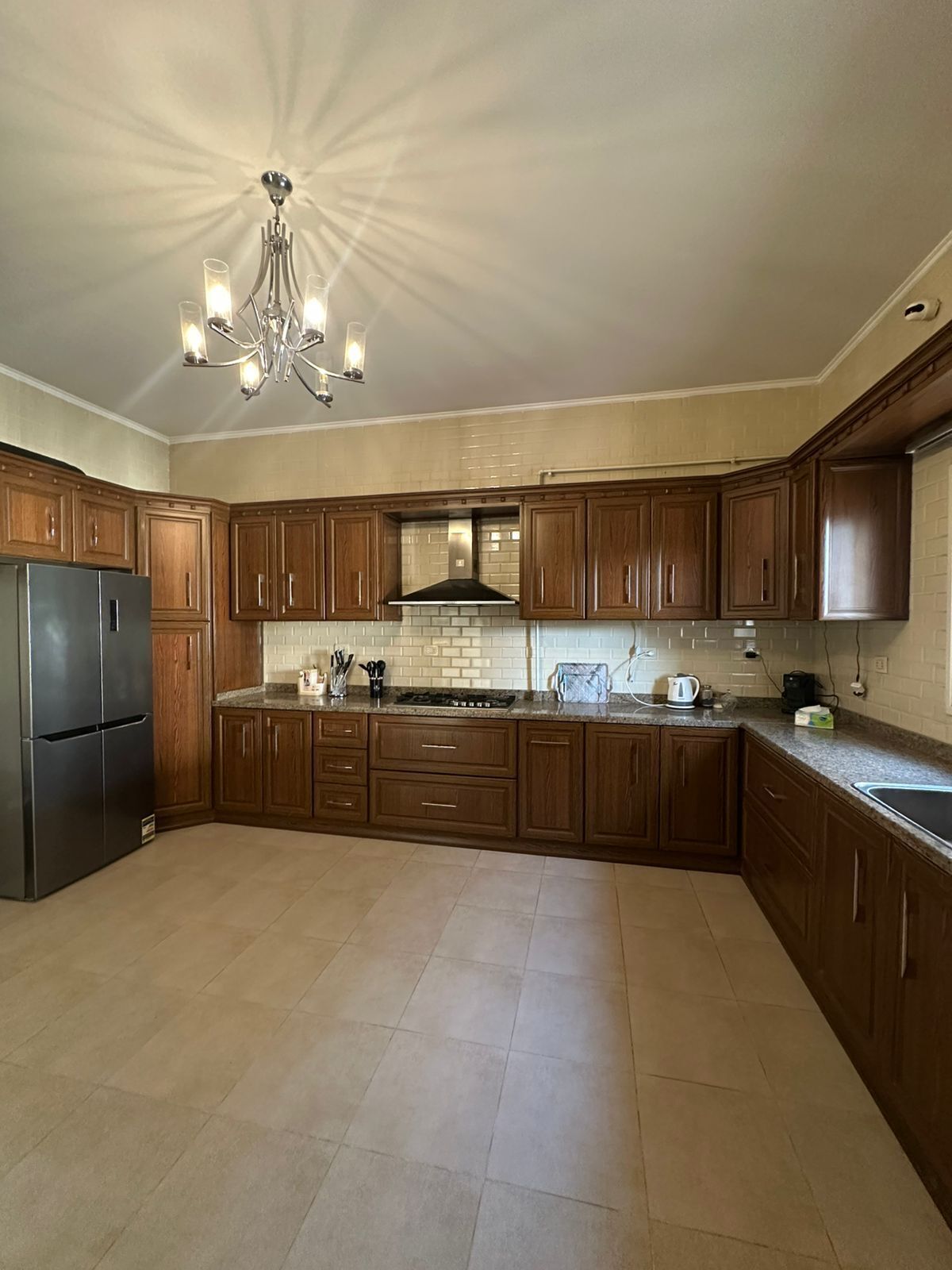 A kitchen with wooden cabinets, a stainless steel refrigerator, a built-in stove, and a chandelier.