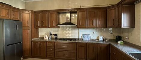 A kitchen with wooden cabinets, a stainless steel refrigerator, a built-in stove, and a chandelier.