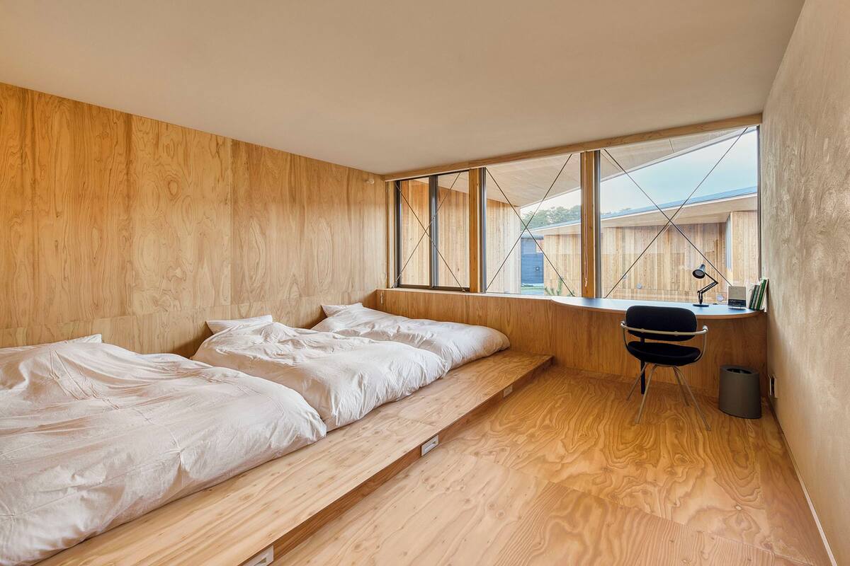A bedroom with a wooden floor, a bed, a desk, and a chair.