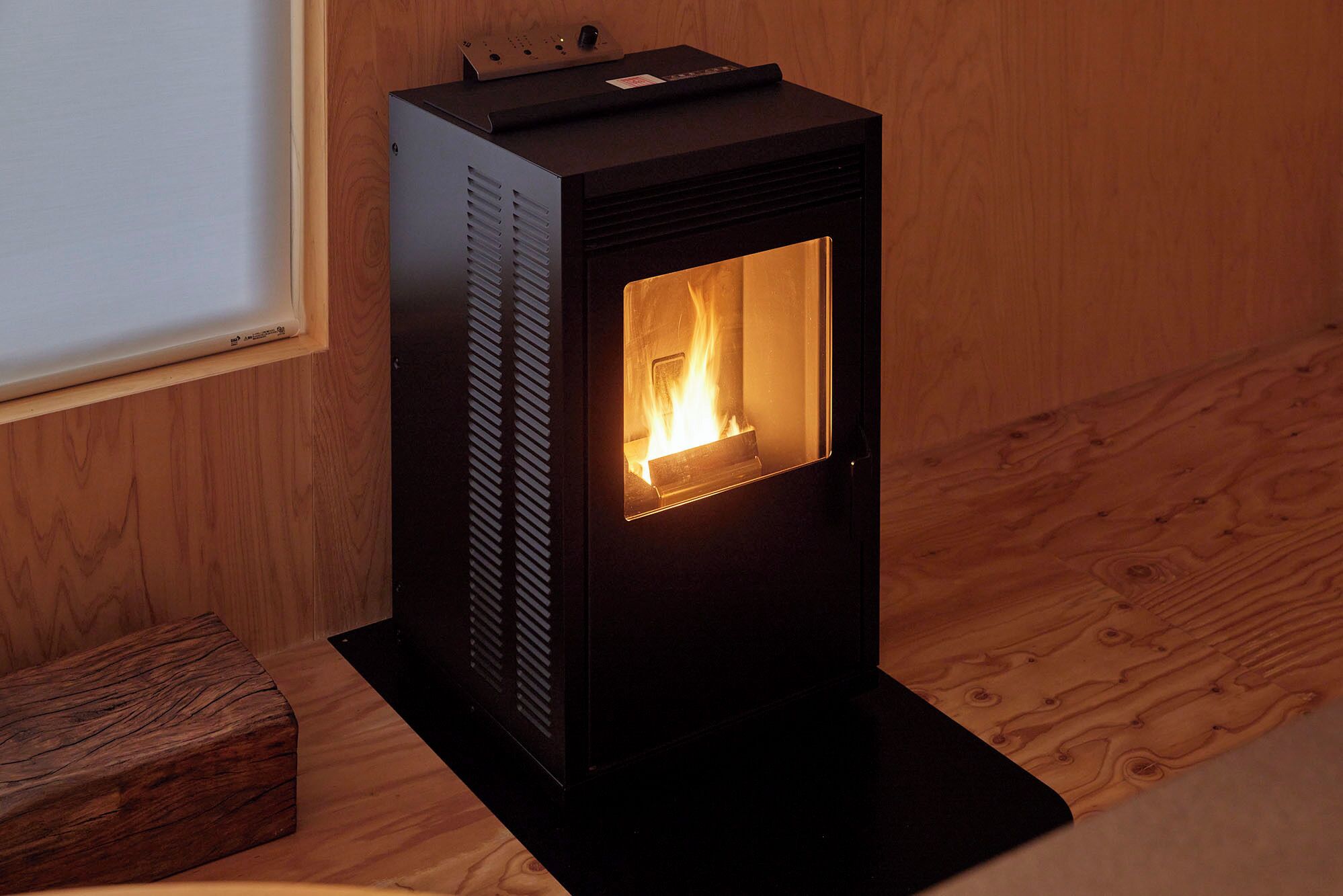 A wood-burning stove with a glass door, a control panel, and a wooden floor.