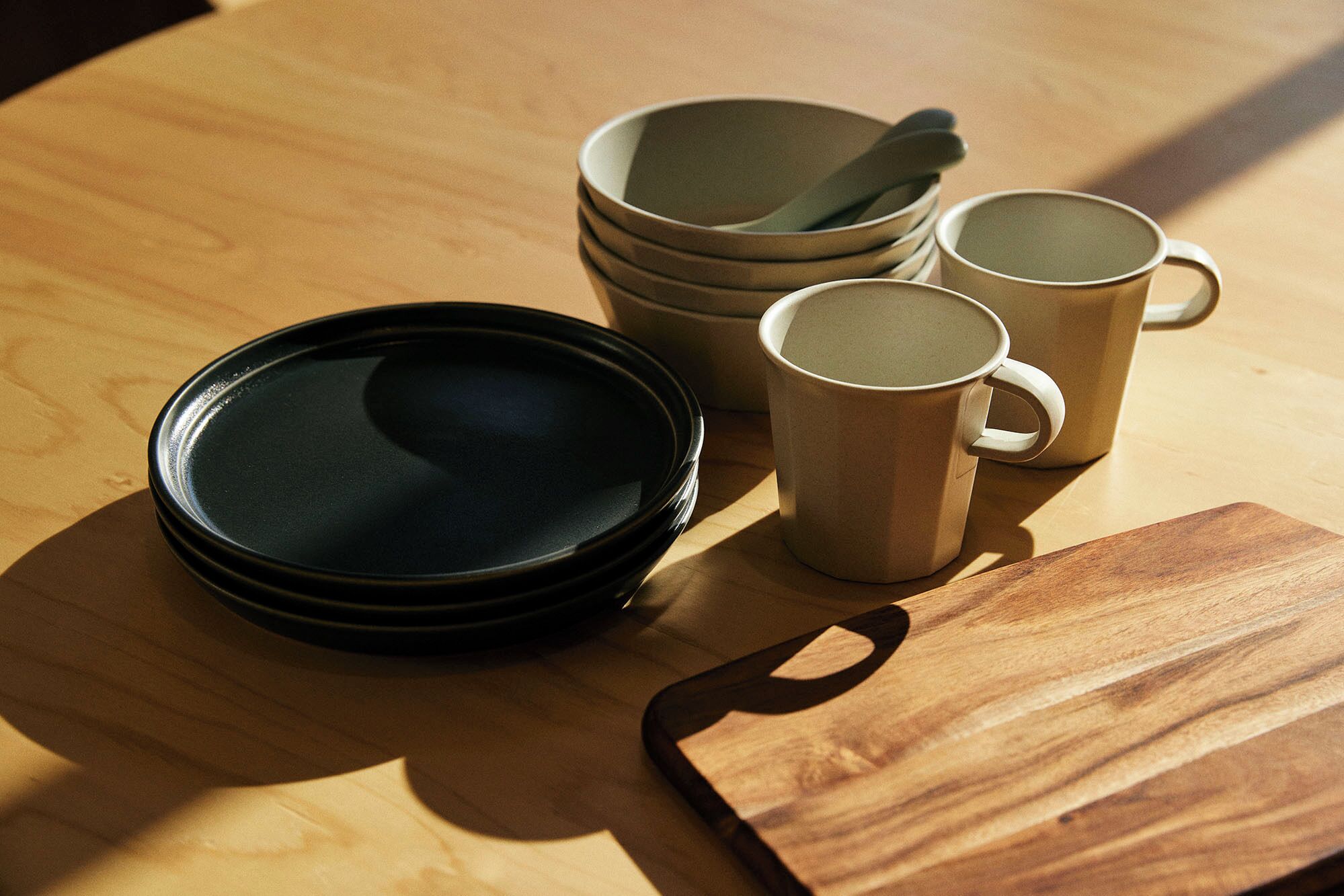 Un montón de platos, un tazón y dos tazas sobre una mesa de madera.