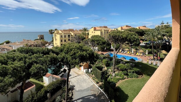 Un hotel costero con piscina, exuberante vegetación y vistas al mar.