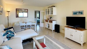 Una sala de estar con un sofá, una mesa de comedor, un televisor, un mueble aparador y un espejo.