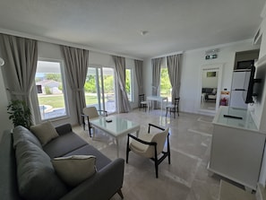 A modern living room with a sofa, a glass coffee table, and a dining area with chairs. - MedVillas Dalyan (Dalyan)