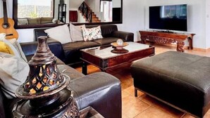 A living room with a sofa, ottoman, coffee table, TV, and a decorative vase. - Villa Bali (Playa Blanca)