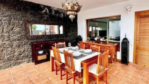 A dining area with a stone wall, wooden dining table, chairs, and a chandelier. - Villa Bali (Playa Blanca)