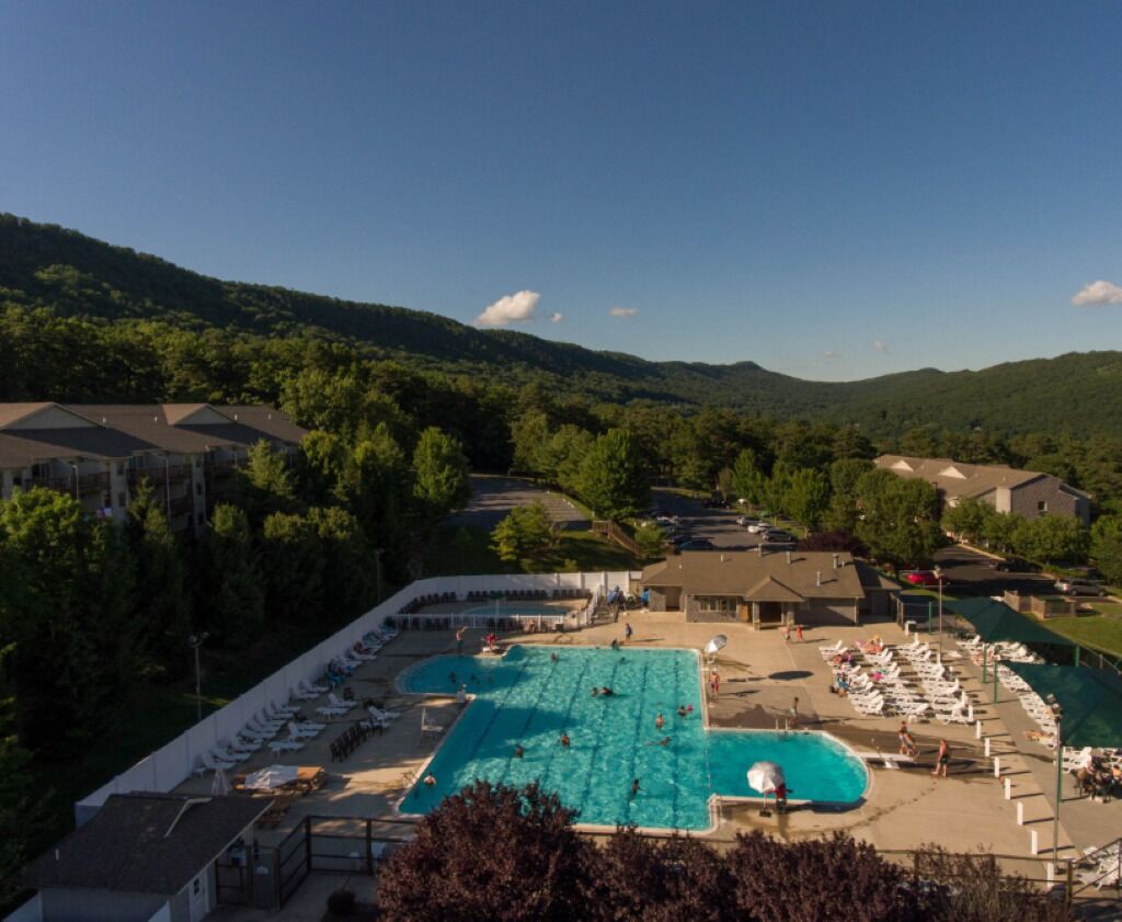 A resort with a large swimming pool, multiple lounge areas, and a mountainous backdrop.