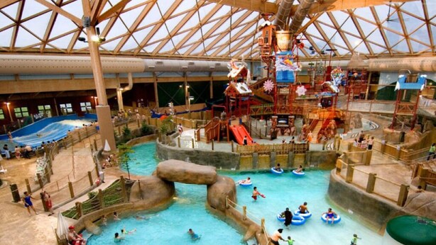 Parque acuático interior con múltiples piscinas, toboganes y zonas de juegos de agua.