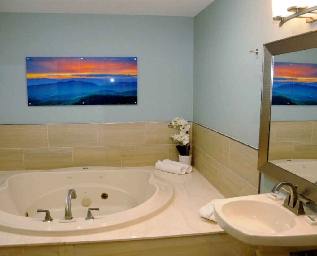A bathroom with a bathtub, a sink, and a mirror. There is a painting on the wall above the bathtub.