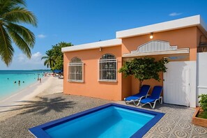 A building with a pool, two lounge chairs, and a view of the beach. - Charming 3-bedroom Apartment in Boca Chica, Dominican Republic (Boca Chica)