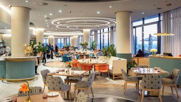 Eine geräumige Hotelhalle mit einer zentralen Sitzecke, großen Fenstern und einem modernen Deckenstil.