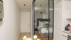 Ein modernes Hotelzimmer mit einer Schiebetür aus Glas zu einem Schlafbereich, einer kleinen Küchenzeile und einem Badezimmer.
