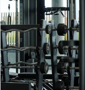 Ein Fitnessraum mit Krafttrainingsgeräten, darunter ein Squat-Rack und Kurzhanteln.