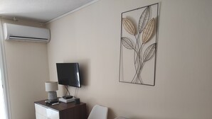 Una habitación con escritorio, televisor, aire acondicionado instalado en la pared y una mesa con mantel estampado.