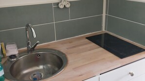 Una cocina con un lavamanos de acero inoxidable, encimera de madera, armarios blancos y salpicadero de azulejos verdes.