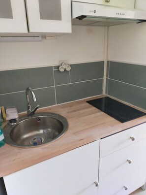 Eine Küche mit Spüle aus Edelstahl, einer Holzausziehtafel, weißen Schränken und einer grünen Fliesenwand.
