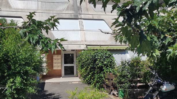 Un edificio con entrada portonada, una motocicleta estacionada y un parterre con flores amarillas.
