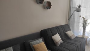 Una sala de estar con un sofá de tono oscuro y estampado, varios cojines, una mesita con un florero y repisas hexagonales en la pared.
