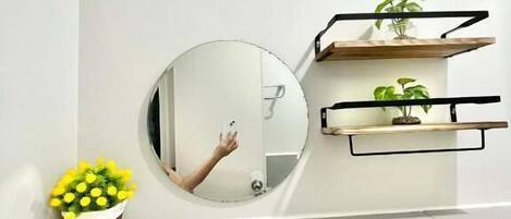 A bathroom with a round mirror, a sink, and two shelves with plants.