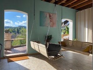 Une pièce avec un fauteuil suspendu, un tableau, un banc en bois et une vue sur la verdure.