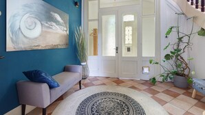 A room with a blue wall, a grey sofa, a patterned rug, a door with glass panels, and a staircase with a railing. - Villa 'theMAP' with Balcony and Wi-Fi (Lenzkirch)