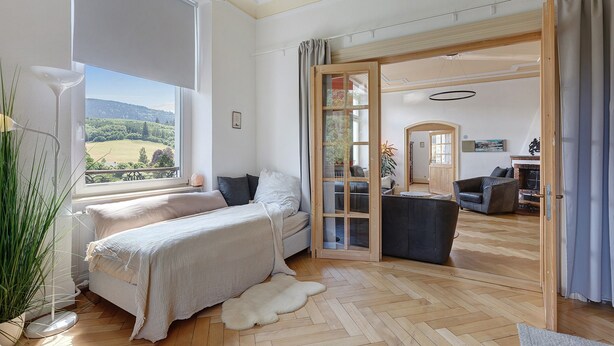 A bedroom with a large window, a bed, a view of the outdoors, and a sliding glass door leading to a living area. - Villa 'theMAP' with Balcony and Wi-Fi (Lenzkirch)