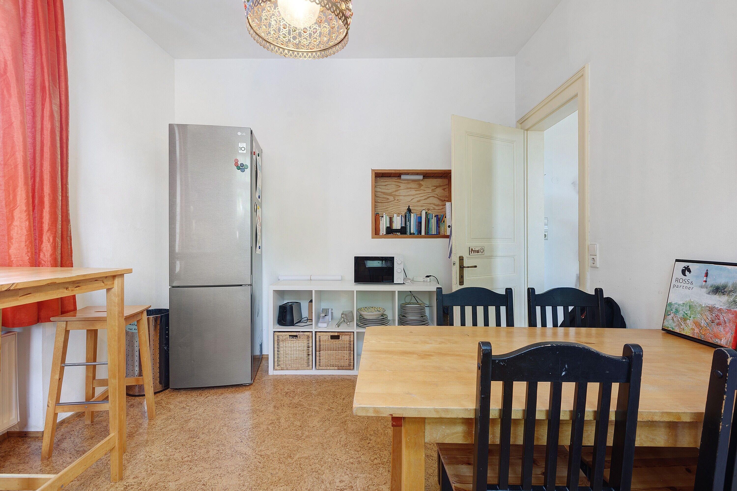 Eine kleine Küche mit Kühlschrank, Mikrowelle und Holzregalen.