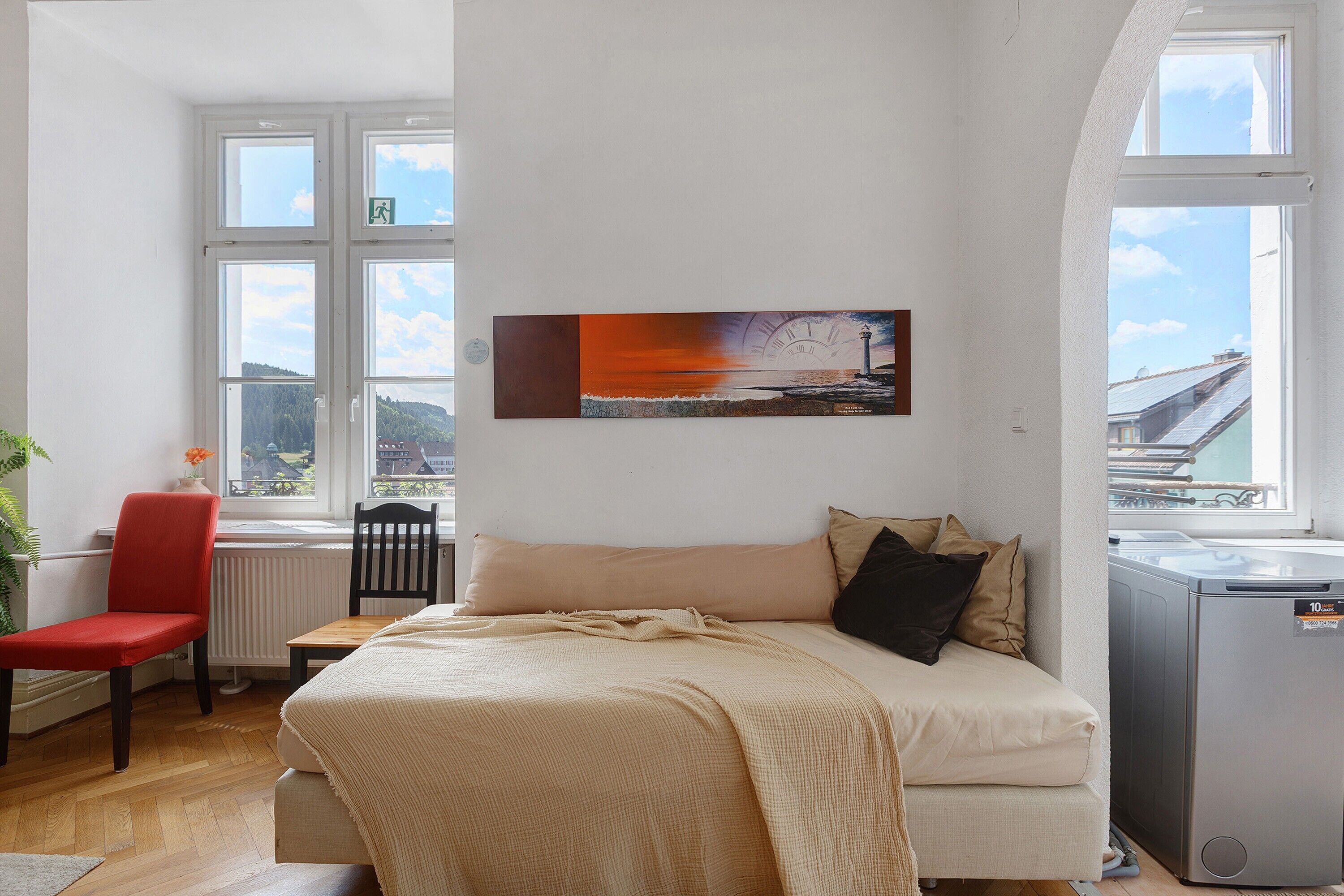 A bedroom with a bed, a chair, a radiator, a window, and a painting.