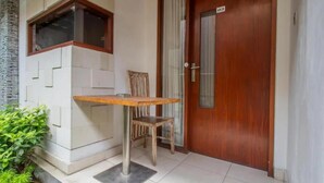 A room with a wooden door, a window, a small table, and a chair. - Cozzy Saren Guesthouse (Kerobokan)