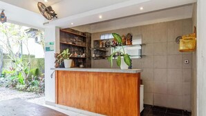 A reception area with a wooden counter, glass shelving with decorative items, and a potted plant. - Cozzy Saren Guesthouse (Kerobokan)
