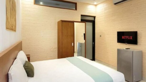 A hotel room with a bed, a TV, a wardrobe, and an air conditioning unit. - Cozzy Saren Guesthouse (Kerobokan)