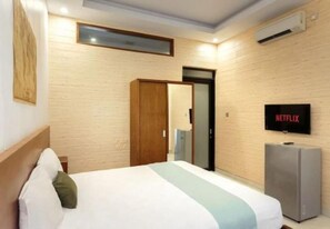A hotel room with a bed, a TV, a wardrobe, and an air conditioning unit. - Cozzy Saren Guesthouse (Kerobokan)