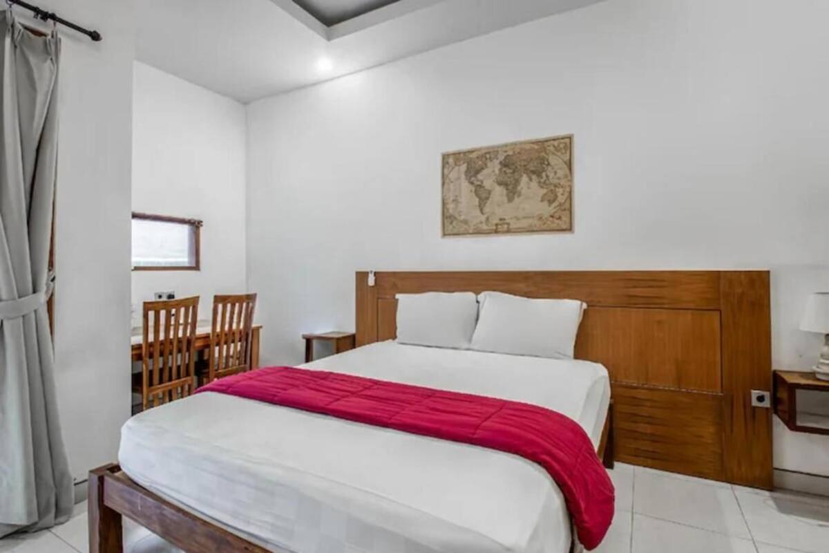 Un dormitorio con cama de madera, una manta roja, un mapa del mundo en la pared, una mesita y una silla.