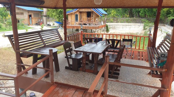 A wooden deck with benches and tables, overlooking a building with a blue roof. - Min Land Resort (Pak Tho)