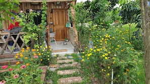 Ein rustikales Holzgebäude mit einer Veranda, umgeben von einem Garten mit Studentenblumen und anderen Pflanzen.