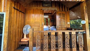 Una baita di legno con un balcone, una ventola e un letto visibile attraverso una porta aperta.