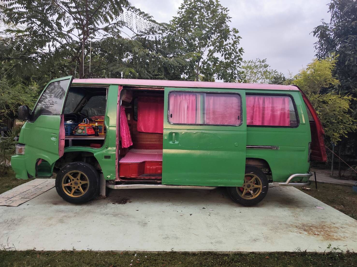 A green van with an open rear door revealing a pink interior, a small storage area, and a rear window.