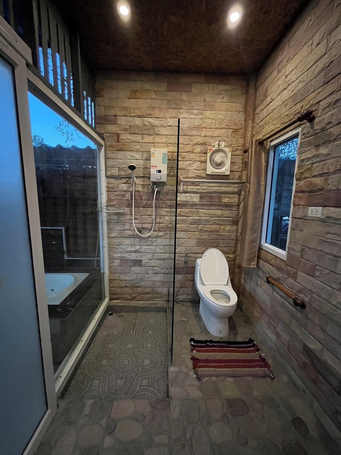 A bathroom with a stone wall, a toilet, a shower, and a glass-enclosed shower area.