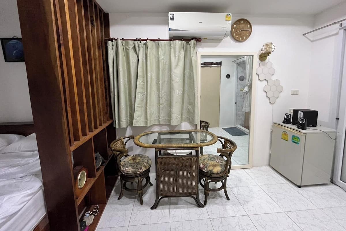 Un espacio habitable compacto con una mesa de comedor, cuatro sillas, un mueble pequeño con altavoces, un reloj y una zona de ducha.