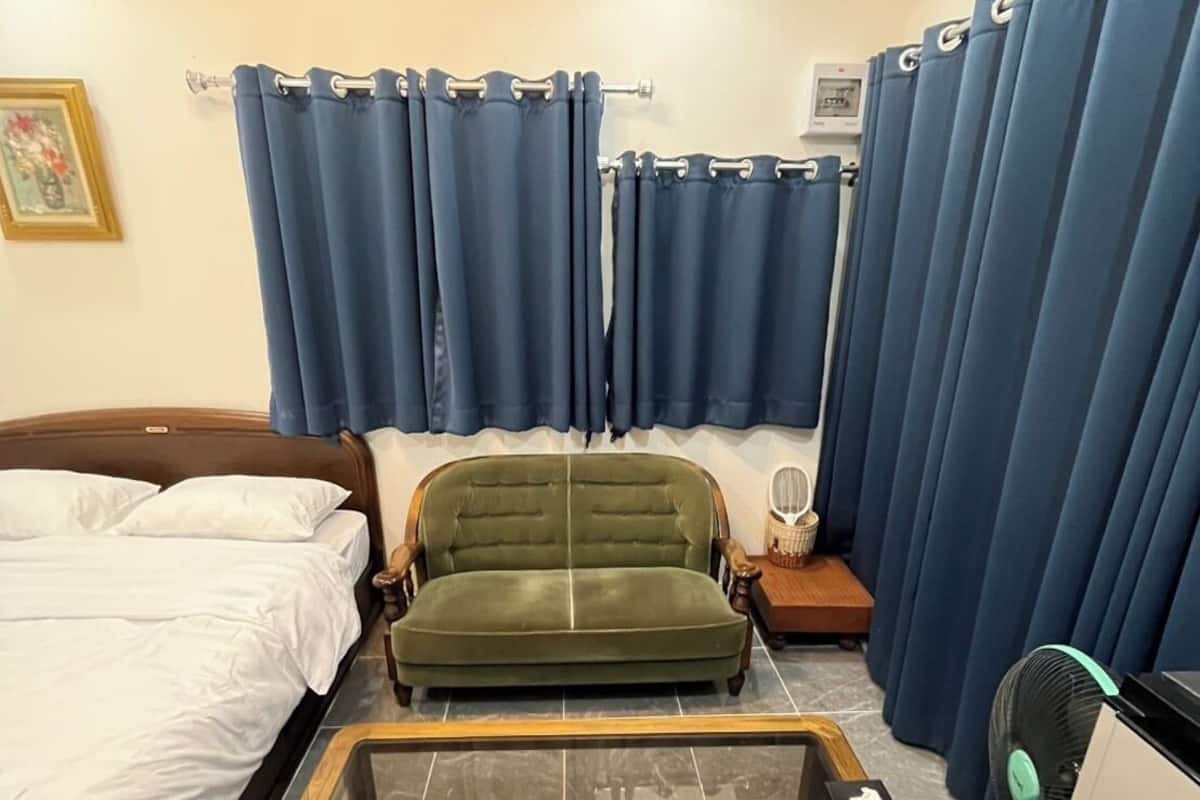 Una habitación de hotel con una cama, un sofá verde, una mesa de centro de vidrio y un escritorio con un ventilador.