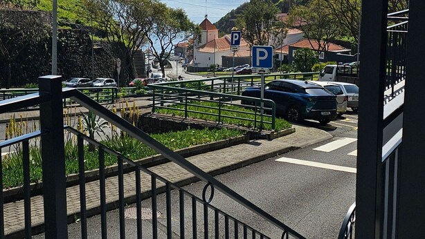 En trappe fører ned til en parkeringsplads med udsigt over havet og bygninger i det fjerne.