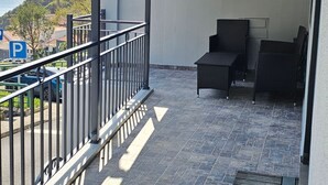 En overdækket balkon med havudsigt, gelænder af metal og to fletstole.