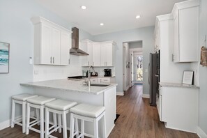 Una cocina moderna con muebles blancos, una isla central con taburetes y vistas al exterior.
